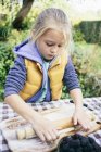 Девочка катит тесто в сельском саду — стоковое фото