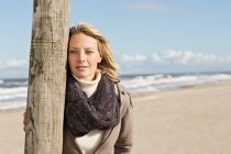 Женщина, опирающаяся на столб на пляже — стоковое фото