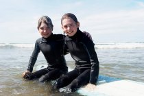 Children sitting on surf board in the se — Stock Photo
