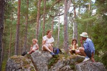 Family sitting on rocks in forest eating picnic — Stock Photo