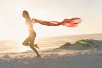 Женщина бежит с саронгом на пляже — стоковое фото