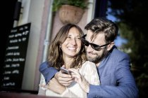 Couple hugging and smiling, using smartphone, Berlin, Germany — Stock Photo