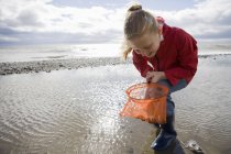 Junges Mädchen schaut in Fischnetz am Strand — Stockfoto
