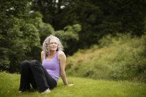 Mature woman taking a break from yoga practice in field — Stock Photo