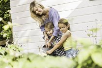 Mulher adulta média e duas filhas regando plantas no jardim — Fotografia de Stock