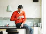 Man using tablet and drinking coffee in kitchen — Stock Photo