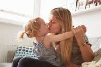 Mitte erwachsene Frau küsst Kleinkind-Tochter auf Sofa — Stockfoto