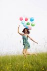 Женщина с воздушными шарами прыгает в поле — стоковое фото