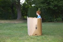 Молодий хлопчик дивиться з картонної коробки в саду — стокове фото