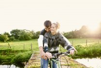 Jeune couple partageant un vélo à la passerelle — Photo de stock