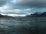 Flooded valley and snowcapped rocks under cloudy sky — Stock Photo