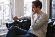 Homme adulte moyen assis sur le canapé, regardant le téléphone intelligent — Photo de stock
