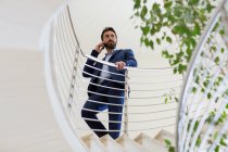 Молодий бізнесмен розмовляє по смартфону на офісних сходах — стокове фото