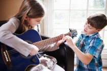 Мальчик помогает девушке играть на гитаре — стоковое фото