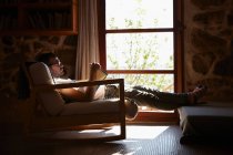 Hombre adulto medio leyendo libro mientras se relaja en la sala de estar - foto de stock