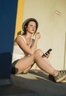 Молода жінка сидить зовні будівлі зі смартфоном — стокове фото