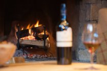 Glass of wine and bottle by fireplace — Stock Photo