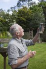 Старший чоловік, що заправляє годівницю для птахів в саду — стокове фото