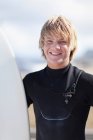 Adolescente surfista segurando bordo na praia — Fotografia de Stock