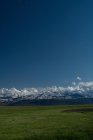 Montagne con campo verde sotto il cielo blu — Foto stock