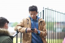 Giovane studente di college maschile lettura di testo smartphone nel campus — Foto stock
