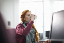 Junge Studentin am Computertisch trinkt Kaffee zum Mitnehmen — Stockfoto