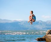 Дівчина стрибає у воду з горами на фоні — стокове фото