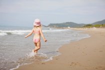 Visão traseira da menina andando em ondas na praia — Fotografia de Stock