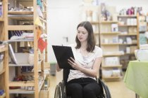 Giovane assistente di negozio femminile che utilizza il bilancio della sedia a rotelle nel negozio — Foto stock