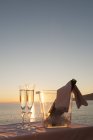 Flûtes à champagne et seau avec bouteille contre le coucher du soleil — Photo de stock