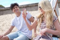 Молодая пара смотрит на смартфон на пляже — стоковое фото