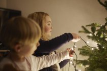 Младшие брат и сестра устанавливают рождественские огни — стоковое фото