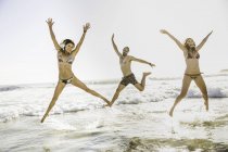 Three adult friends wearing bikini and shorts jumping  in sea, Cape Town, South Africa — Stock Photo