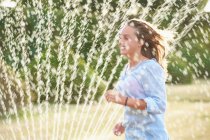 Donna che corre attraverso l'irrigatore — Foto stock