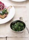 Bowl of cooked spinach and plate with meat in background — Stock Photo