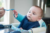 Baby reaching for spoon at table — Stock Photo