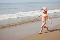 Fille en chapeau de soleil courir sur la plage — Photo de stock