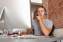 Young man working on computer wearing headphones — Stock Photo