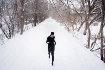 Young female runner in knit hat running in snow covered tree lined park — Stock Photo
