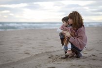 Мати і дочка, загорнуті в ковдру, обіймаються на пляжі — стокове фото
