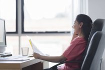 Frau hält Papiere und sitzt am Arbeitstisch und telefoniert mit dem Handy — Stockfoto