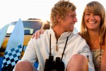 Paar sitzt lächelnd mit Lieferwagen am Strand — Stockfoto