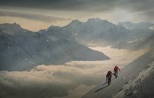 Dos escaladores en una ladera nevada sobre un mar de niebla en un valle alpino, Alpes, Cantón Wallis, Suiza - foto de stock