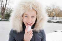 Дівчина в хутряному капюшоні лиже сніг — стокове фото