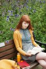 Jeune rousse femme lecture sur banc — Photo de stock