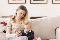 Mutter hält Baby mit Smartphone zu Hause — Stockfoto
