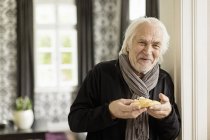 Senior man holding danish pastry — Stock Photo