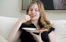 Девочка-подросток ест на диване — стоковое фото