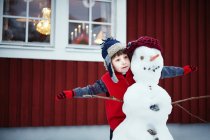 Garçon jouer avec bonhomme de neige à l'extérieur — Photo de stock