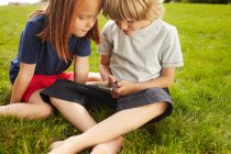 Enfants utilisant un téléphone portable dans l'herbe — Photo de stock